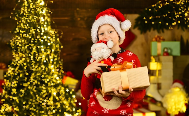 Le Père Noël m'a apporté des cadeaux. Tradition de décembre. Remise de vente. Un vrai bonheur. Enfant heureux excité près de l'arbre de Noël. Joyeux Noël. Concept d'enfance heureuse. L'enfant porte un bonnet de noel et un pull de noël.