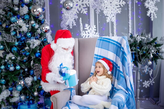 Le Père Noël offre un cadeau à une petite fille à l'arbre de Noël