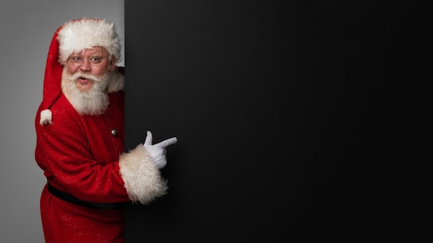 Père Noël pointant sur un panneau d'affichage en papier noir avec espace de copie pour le texte