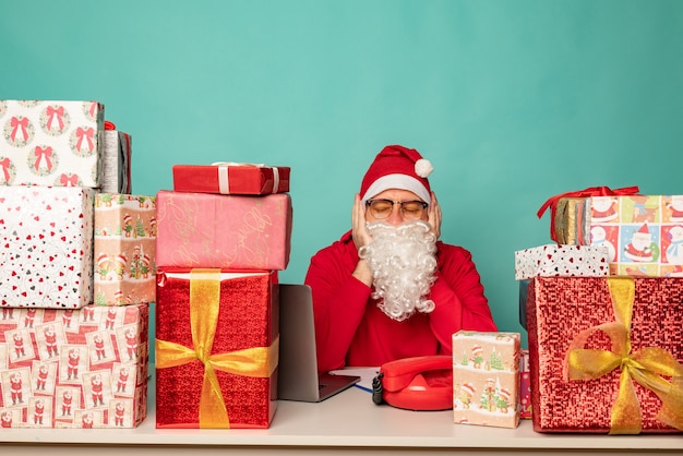 Le Père Noël portant un chapeau travaille dans son bureau avec des cadeaux, se préparant pour les vacances.