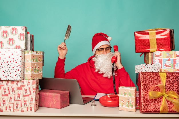 Le Père Noël portant un chapeau travaille dans son bureau avec des cadeaux, se préparant pour les vacances.