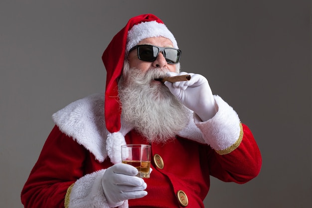 Père Noël portant des lunettes de soleil fumant un cigare et buvant un fouet sur fond sombre