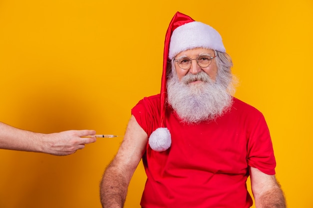 Le Père Noël portant un masque facial se fait vacciner par injection