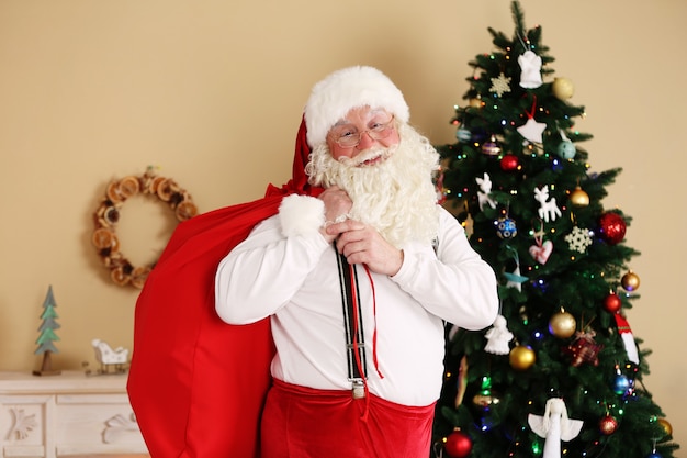 Père Noël avec sac de cadeaux près de l'arbre de Noël à la maison