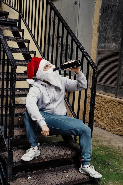 Le Père Noël sans abri boit du vin et fouille dans les poubelles.