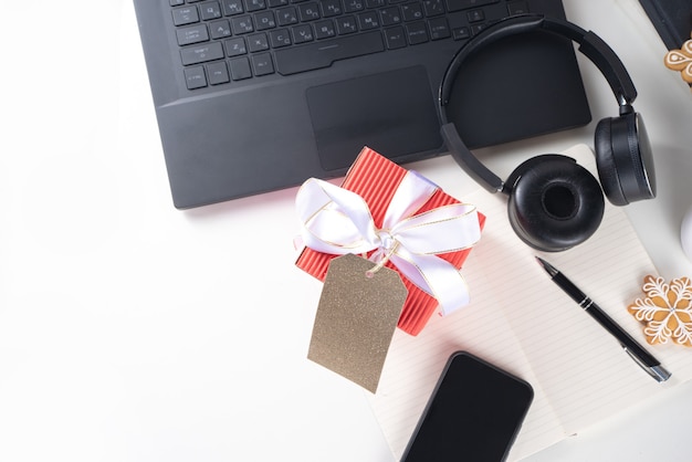 Père Noël secret. Célébration de Noël au bureau. Bureau avec ordinateur portable, bloc-notes, fournitures de bureau, smartphone et grand coffret cadeau de Noël avec noeud festif. flatlay