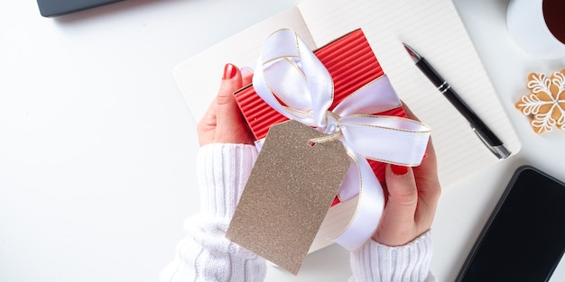 Père Noël secret. Fête de Noël au bureau. Bureau avec ordinateur portable, blocs-notes, fournitures de bureau, smartphone et grande boîte-cadeau de Noël avec nœud festif. espace de copie flatlay