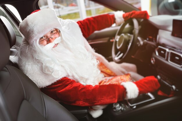 Le Père Noël sourit avec ses mains sur le volant d'une nouvelle voiture