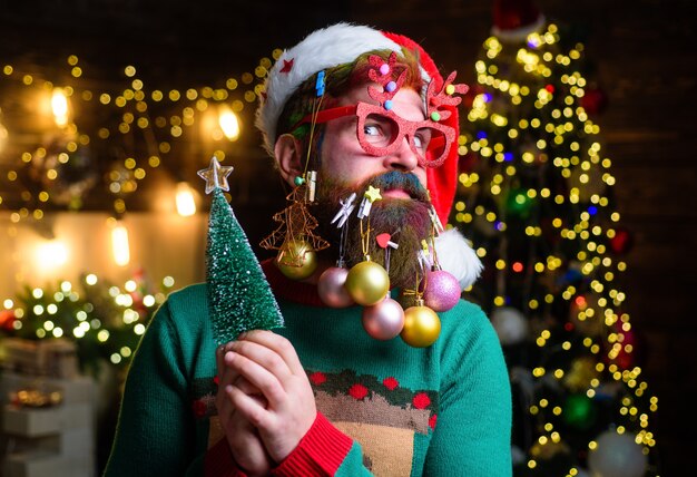 Le père noël surpris avec des boules du nouvel an dans la barbe tient un sapin de noël de style barbe de noël