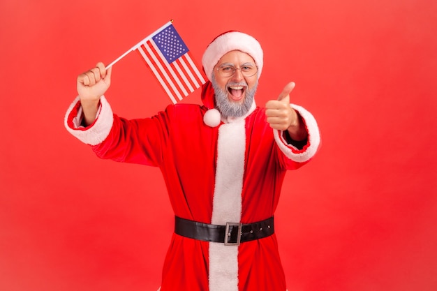 Père Noël tenant le drapeau des États-Unis, montrant le pouce vers la caméra, d'humeur patriotique.