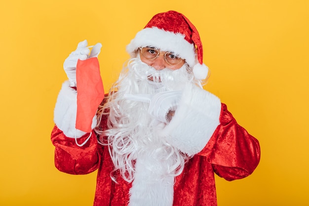 Père Noël tenant un masque rouge, sur jaune