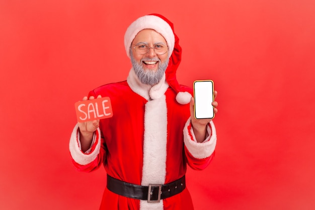 Père noël tenant un smartphone avec affichage vierge et carte de vente en mains, application de remise.