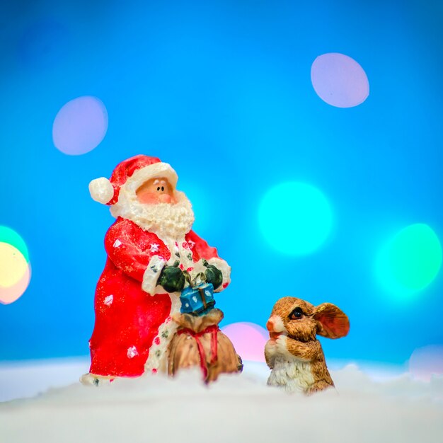 Père Noël en tenue rouge avec un lapin dans la neige sur fond bleu avec éclairage