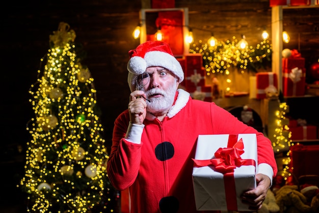 Le père noël tient le présent vous souhaite joyeux noël homme souriant en bonnet de noel tenir présent boîte-cadeau