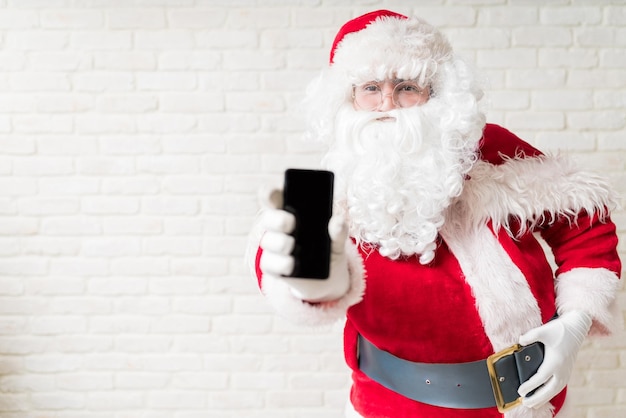 Le Père Noël tient son téléphone portable alors qu'il est à la maison.