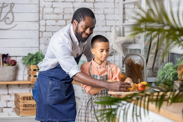 Père noir et son fils enfant cuisinant des légumes frais dans la cuisine à la maison père africain et garçon enfant p