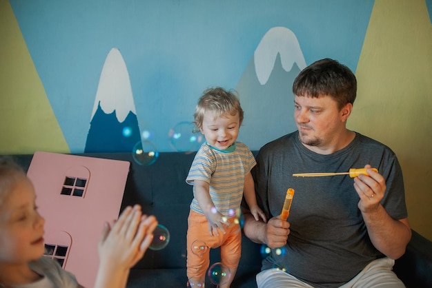 Un père avec de nombreux enfants s'amuse à jouer avec ses petits enfants à la maison en soufflant des bulles de savon