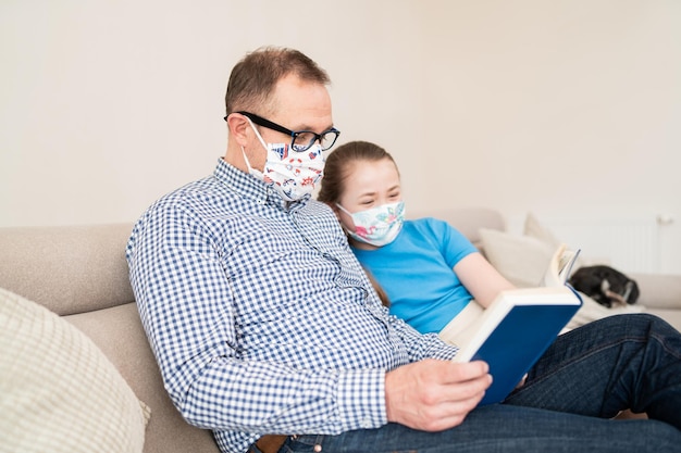 Le père passe du temps libre avec l'enfant pendant la quarantaine papa en masque médical sur son visage lit un livre