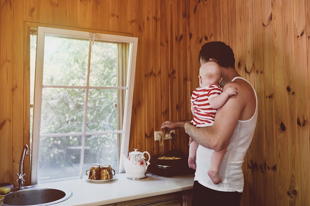 Père avec un petit bébé dans ses bras prépare le dîner