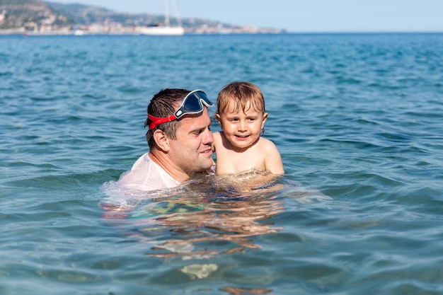 Père et petit fils s'amusant à nager et à jouer ensemble dans l'eau de mer pendant les vacances d'été