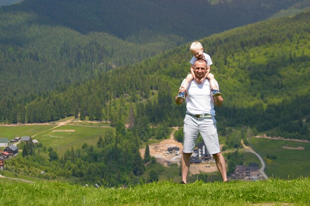 Père avec un petit fils sur ses épaules. Montagnes. Journée d'été ensoleillée.