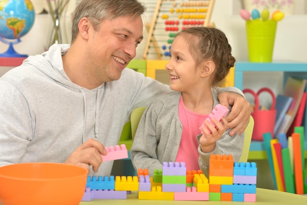 Père et petite fille mignonne assis à table et jouant avec des blocs de plastique colorés