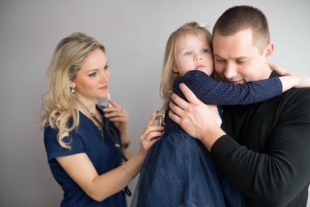 Un père porte sa jolie fille pendant que le pédiatre l'examine sur un fond gris.