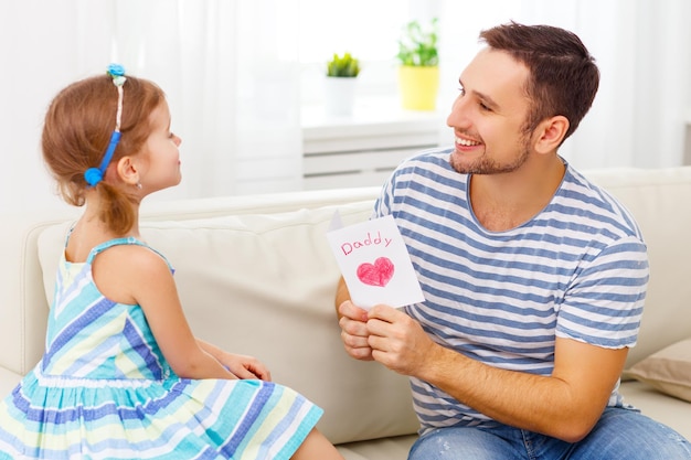 Un père et sa fille sont assis sur le canapé et tiennent une carte qui dit tous les jours