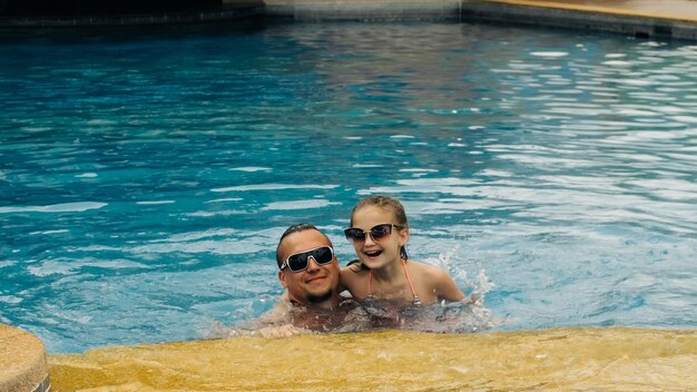 Le père avec sa petite fille s'amuse dans la piscine Papa joue avec l'enfant La famille profite des vacances d'été dans une piscine Ralenti