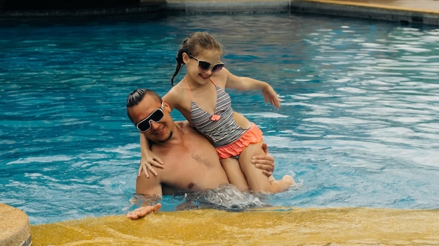 Le père avec sa petite fille s'amuse dans la piscine Papa joue avec l'enfant La famille profite des vacances d'été dans une piscine en sautant en tournant l'eau des éclaboussures Ralenti