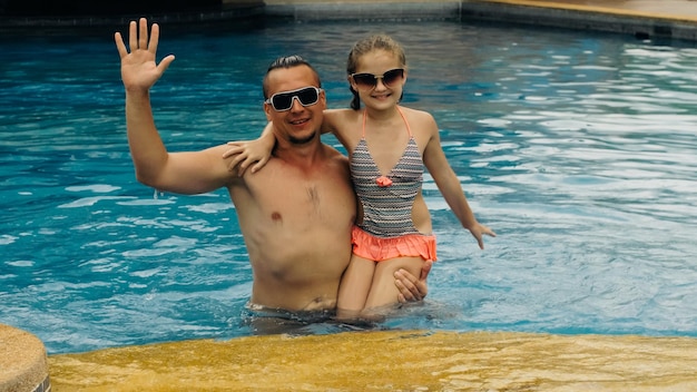 Le père avec sa petite fille s'amuse dans la piscine. Papa joue avec l'enfant. La famille profite des vacances d'été dans une piscine en sautant, en tournant, en éclaboussant l'eau. Ralenti.