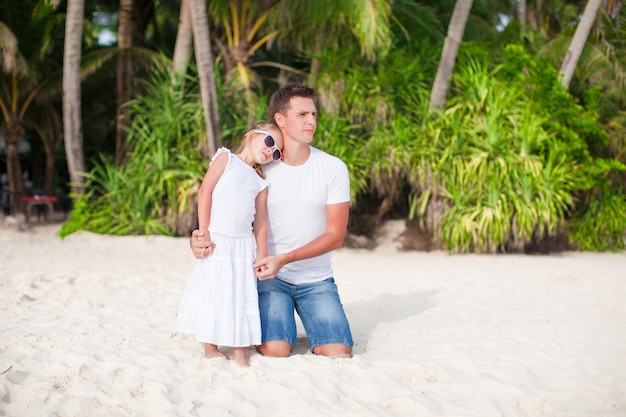 Père avec sa petite fille se détendre sur la plage blanche
