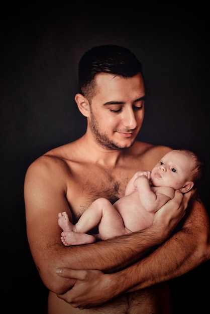 Un père sans chemise avec un bébé sur un fond noir