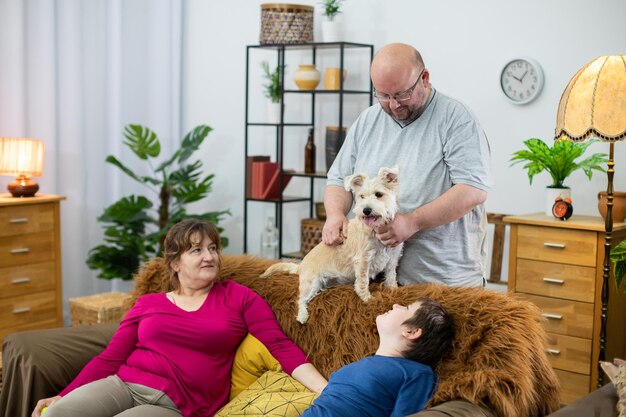 Le père se tient derrière le canapé et caresse le chien poilu le reste de la famille regarde tout le plaisir