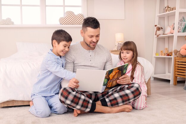 Père et ses petits enfants lisant l'histoire du coucher à la maison