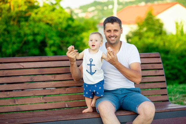 Un père et son bébé se promènent dans le parc en été au soleil couchant et sourient tout en s'amusant