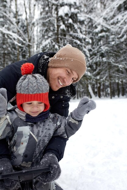 Père et son fils au chapeau drôle s'amusant et riant dans la forêt d'hiver enneigée Famille heureuse portant des vêtements d'hiver chauds profitant de l'hiver dans la pinède enneigée Activités de plein air avec les enfants