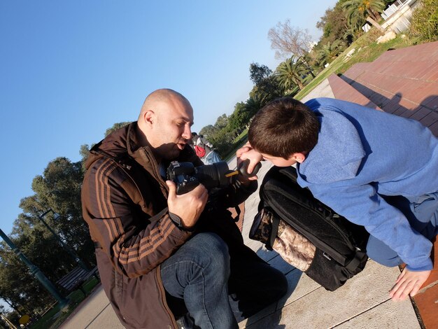 Un père et son fils nettoient l'objectif d'une caméra avec un souffleur de poussière d'air dans un parc.