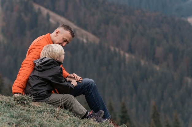 Père et son fils s'assoient sur la pente et regardent les montagnes Trekking en famille avec des enfants en forêt