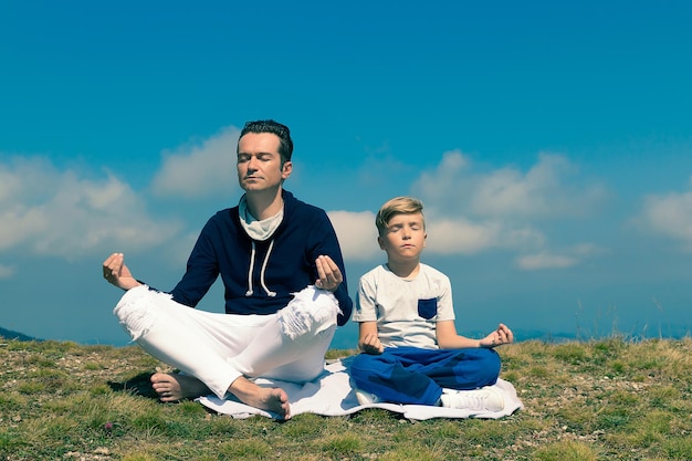 Photo un père et son fils zen méditant sur un pré et un sommet de montagne contre le ciel.