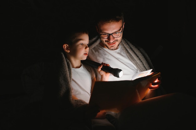 Père et son petit fils lisant une histoire au coucher à la maison