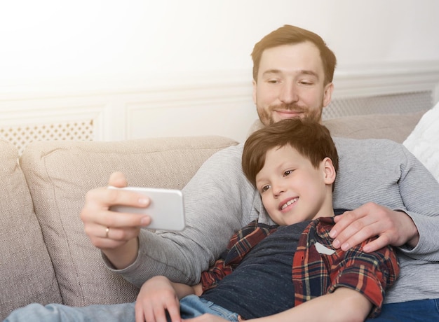 Père et son petit fils prenant une photo de selfie avec un smartphone à la maison