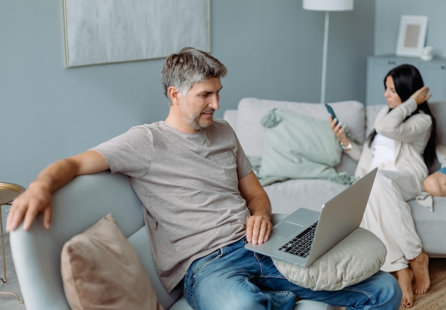 Père souriant à l'aide d'un ordinateur portable dans un salon confortable