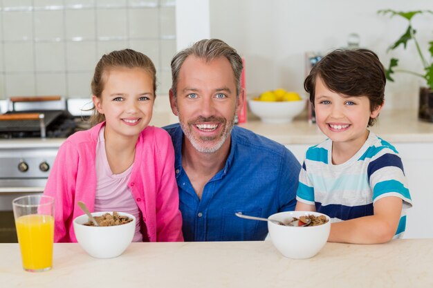 Père souriant et enfants prenant son petit déjeuner dans la cuisine