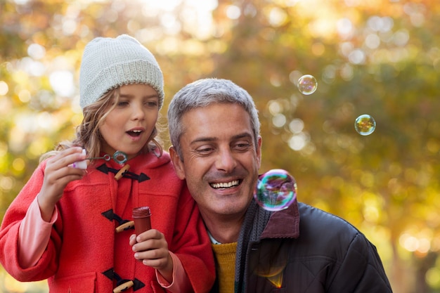 Père souriant avec fille soufflant des bulles au parc