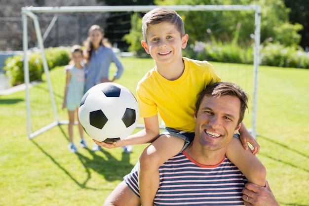 Père souriant portant son fils sur l'épaule au parc