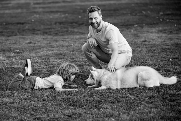 Un père souriant et son fils jouant avec un chien dans un parc avec un enfant de compagnie marchent avec un chien