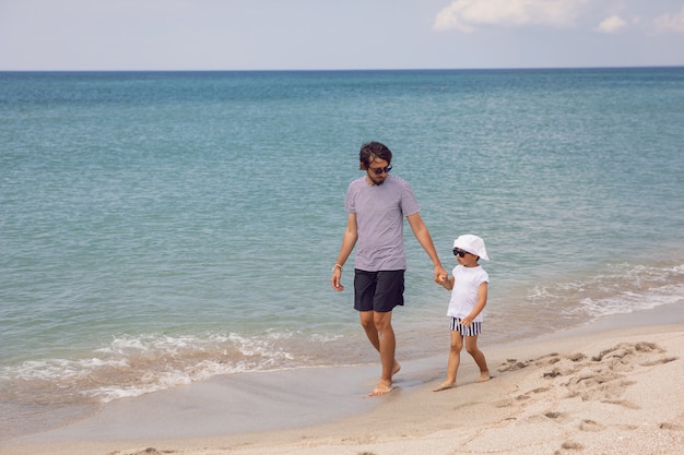 Un père en T-shirt rayé marche avec son fils en short et un T-shirt marchant sur la plage en été pendant les vacances