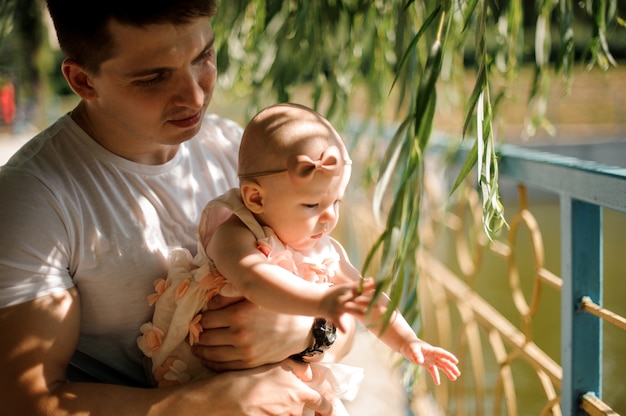 Père tenant sa petite fille sur les mains amotng les feuilles de saule