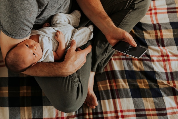 Père tenant son bébé tout en utilisant son téléphone